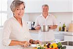 Old couple smiling preparing food in kitchen