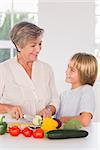 Grandmother cutting vegetables looking at grandson in kitchen