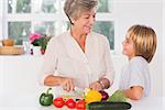 Grandmother cutting vegetables looking at her grandson in kitchen