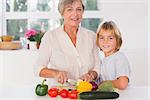 Grandmother cutting vegetables with her grandson in kitchen