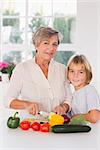 Granny cutting vegetables with her grandson in kitchen