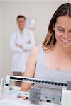 Woman weighing herself being supervised by doctor