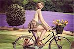 pretty blonde woman going  on the bicycle with colourful flowers in the basket. She wearing pink tank and very short floral skirt. rural field lavander