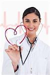 Happy doctor holding up stethoscope to heart design on ECG background