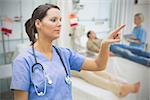 Nurse in blue scrubs standing in hospital ward pointing to something