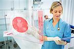 Nurse consulting tablet with screen displaying ECG in foreground in hospital ward