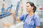 Nurse touching screen showing blue DNA helix data in hospital ward
