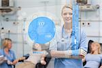 Smiling nurse standing behind blue ECG display screen in hospital ward