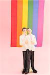 Gay groom cake toppers in front of rainbow flag on pink background