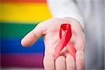 Man holding red awareness ribbon on rainbow background
