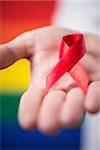 Man holding red aids awareness ribbon close up on rainbow background