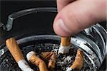 Hand putting out a cigarette in ashtray on black background