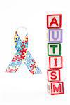 Autism awareness ribbon beside stacked blocks spelling autism on white background