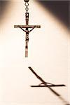 Cross hanging from rosary beads casting a shadow
