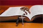 Rosary beads resting on open bible on wooden table