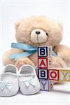 Blocks spelling baby boy with teddy and baby shoes on white background