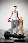 Female boxer standing on black chess piece on chessboard