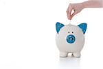 Hand placing coin into blue and white piggy bank on white background