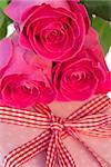 Pink roses resting on pink polka dot wrapped present with gingham ribbon