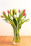 Vase of pink yellow and white tulips on wooden table