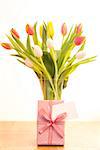 Vase of pink white and yellow tulips on wooden table with gift and blank card