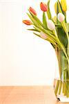 Glass vase of pink yellow and white tulips on wooden table