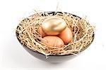 Three eggs in a black bowl with one gold one with straw