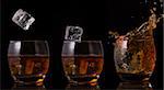 Serial arrangement of ice falling into whiskey glass on black background