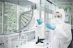 Chemist in protective suit working with futuristic interface with dna diagram on it