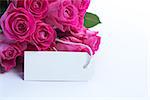 Bouquet of beautiful pink roses with an empty card on a white table