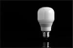 Energy saving bulb standing on black background over a reflective surface