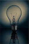 Big clear light bulb standing on reflective surface over dark background