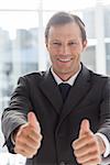 Smiling confident businessman giving thumbs up in his office