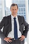 Smiling businessman with his hands on hips in his office