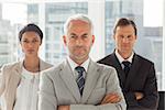 Serious businessman standing with colleagues behind with arms folded