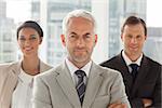 Businessman standing with colleagues behind with arms crossed