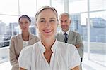 Smiling businesswoman standing in front of colleagues with arms crossed