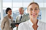 Cheerful businesswoman standing with colleagues working behind on a folder