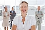 Cheerful businesswoman standing with arms folded in front of colleagues