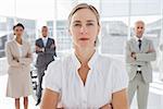 Serious businesswoman standing with arms folded with colleagues behind