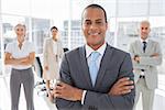 Smiling businessman with arms crossed standing in front of colleagues