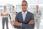 Serious businessman standing with arms crossed in front of colleagues