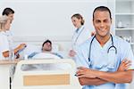 Attractive doctor with arms crossed standing in front of medical team taking care of a patient