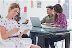 Editor holding tablet and smiling as her team works behind her at a desk in office