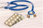 Blue stethoscope laying on ECG results with pills