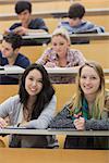 Smiling students sitting in a lecture hall while taking notes