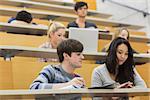 Students working while sitting in a lecture hall with two looking at tablet computer