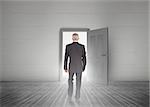 Businessman walking towards door showing light in a dull grey room