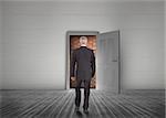 Businessman walking towards door open but blocked by red brick wall in a dull grey room