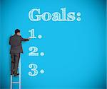 Businessman writing goals on a giant blue wall helped by a ladder